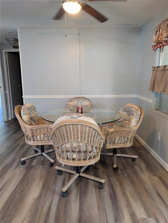 A dining area features a glass-topped table with four wicker rolling chairs on wood-look flooring — 7111 142ND AVENUE N Lot 101, LARGO, FL