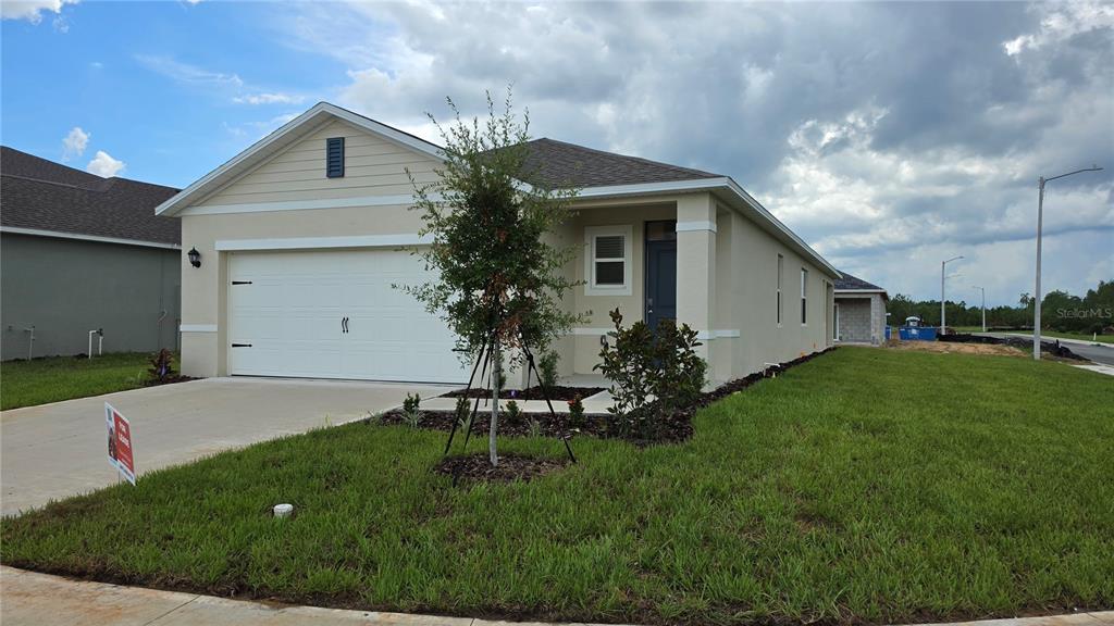 A single-story house with a white garage door, beige siding, and a small front lawn — 4075 LIMEKLIN FALLS LOOP, DAVENPORT, FL