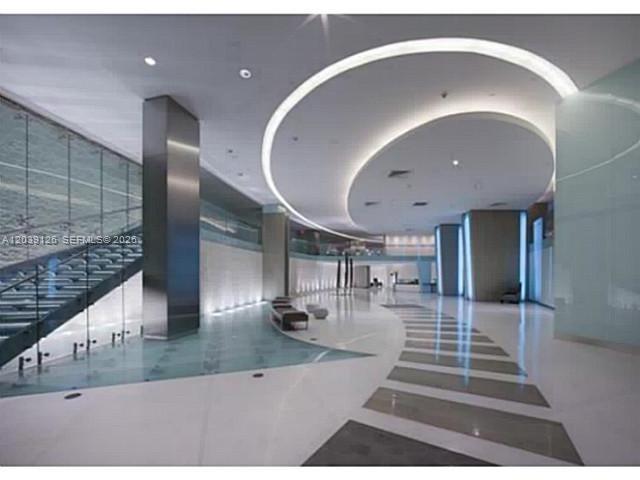 A modern, spacious lobby features a curved ceiling, glass staircase, and polished white tile floors — 92 SW 3rd St # 503, Miami FL 33130, MIAMI, FL
