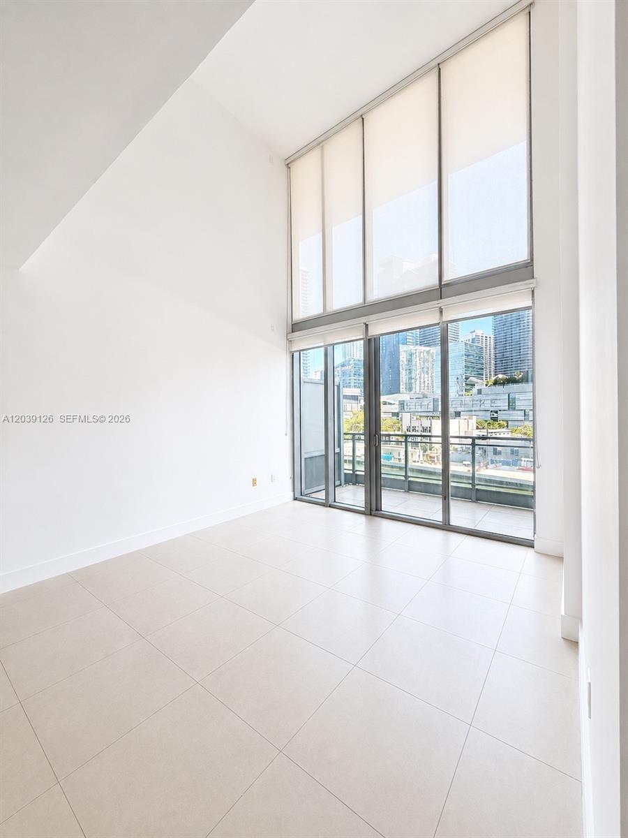 A bright, empty room features high ceilings, large floor-to-ceiling windows, and light-colored tile flooring — 92 SW 3rd St # 503, Miami FL 33130, MIAMI, FL