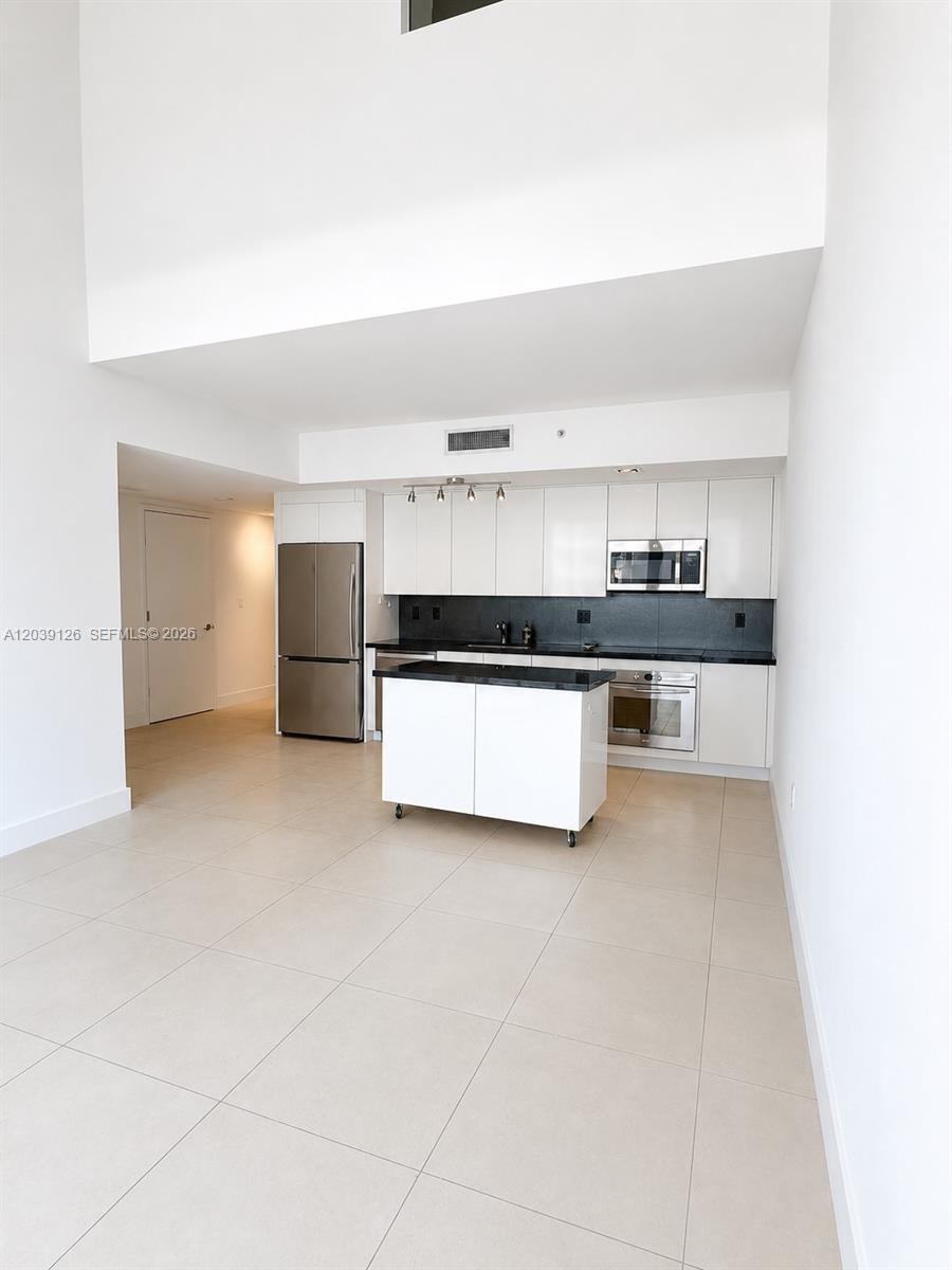 A modern kitchen features white cabinetry, stainless steel appliances, a rolling island, and tile flooring — 92 SW 3rd St # 503, Miami FL 33130, MIAMI, FL