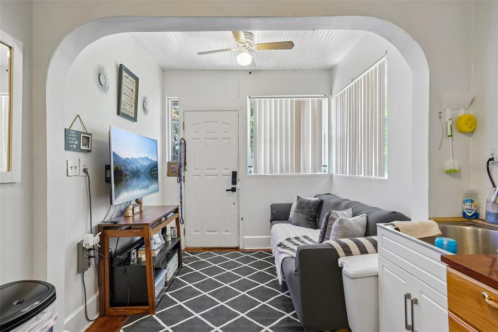 A small living room features a grey sofa, a television on a stand, and white walls — 1028 8TH AVENUE S, ST PETERSBURG, FL