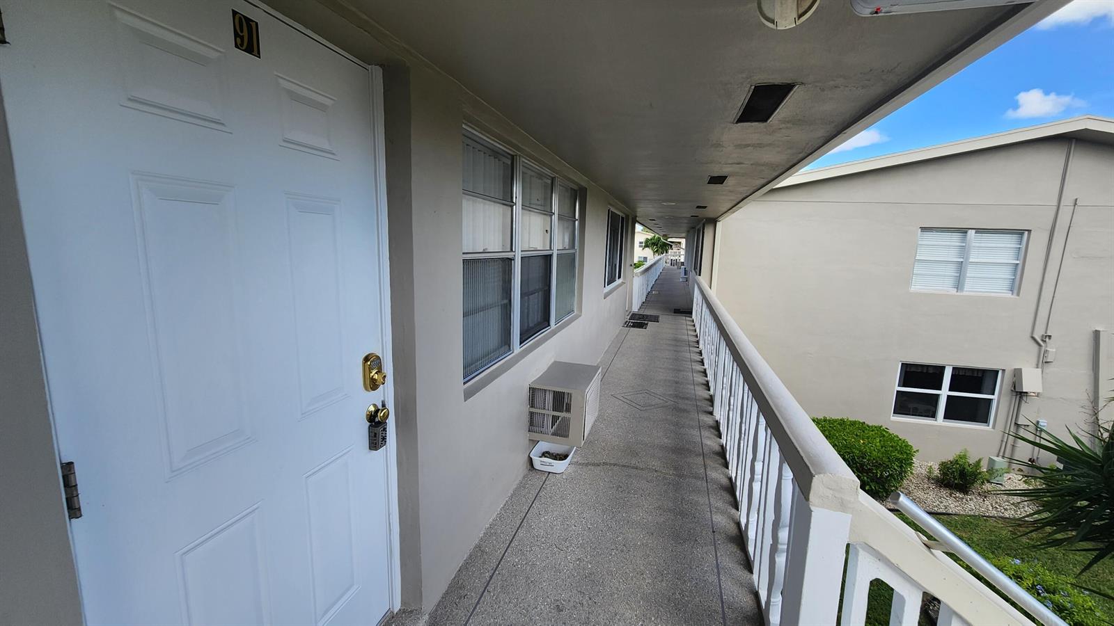 An exterior walkway leads past a white door labeled 91 toward a neighboring building — 91 Coventry D, West Palm Beach FL 33417, WEST PALM BEACH, FL