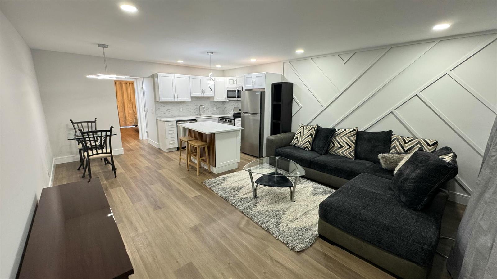 An open-concept living room and kitchen feature white cabinetry, a kitchen island, and wood flooring — 91 Coventry D, West Palm Beach FL 33417, WEST PALM BEACH, FL