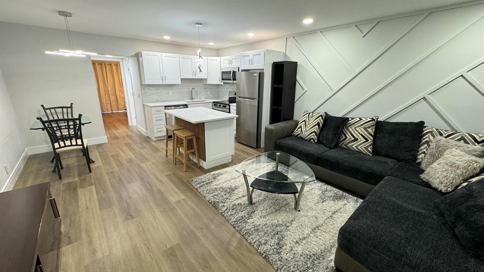 An open-concept living room and kitchen featuring a dark sectional, island, and wood-look flooring — 91 Coventry D, West Palm Beach FL 33417, WEST PALM BEACH, FL