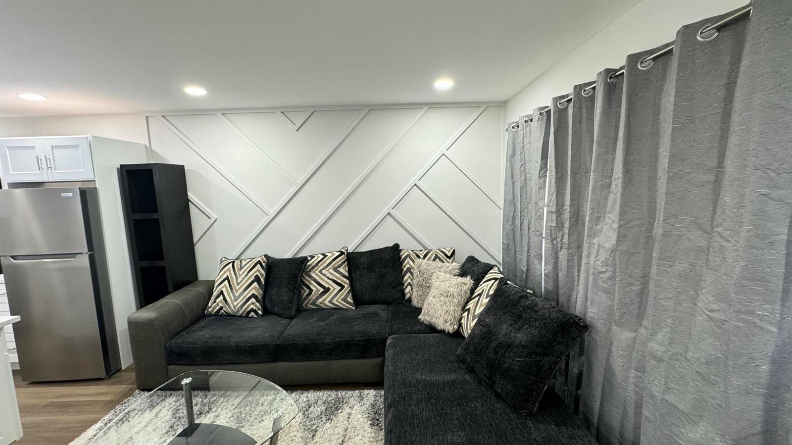 A living room features a dark sectional sofa, a geometric accent wall, and grey curtains — 91 Coventry D, West Palm Beach FL 33417, WEST PALM BEACH, FL