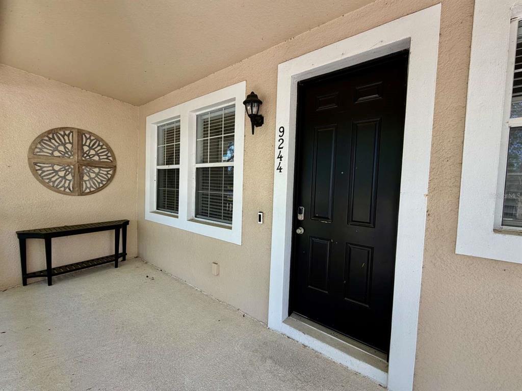 A covered front porch features a black door, a console table, and wall decor — 9244 CARDINAL MEADOW TRAIL, ORLANDO, FL