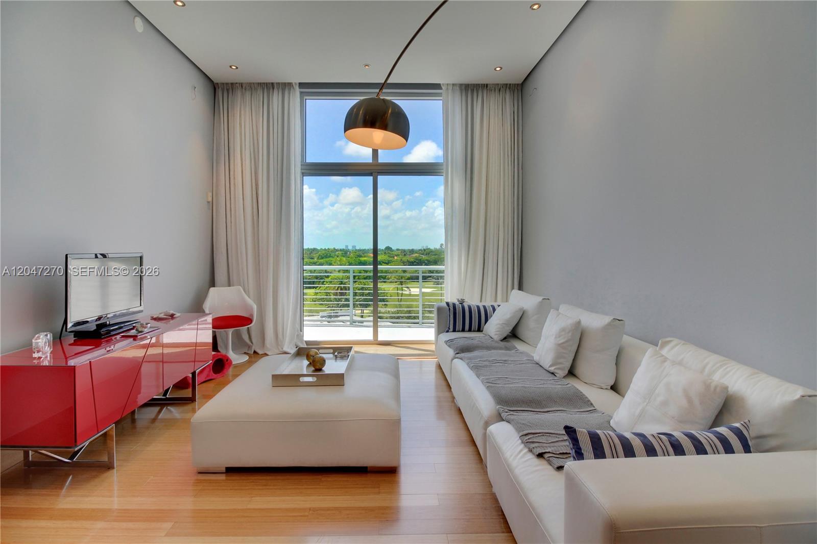 A modern living room features a white sofa, red media console, and floor-to-ceiling window view — 2001 Meridian Ave # 21, Miami Beach FL 33139, MIAMI BEACH, FL