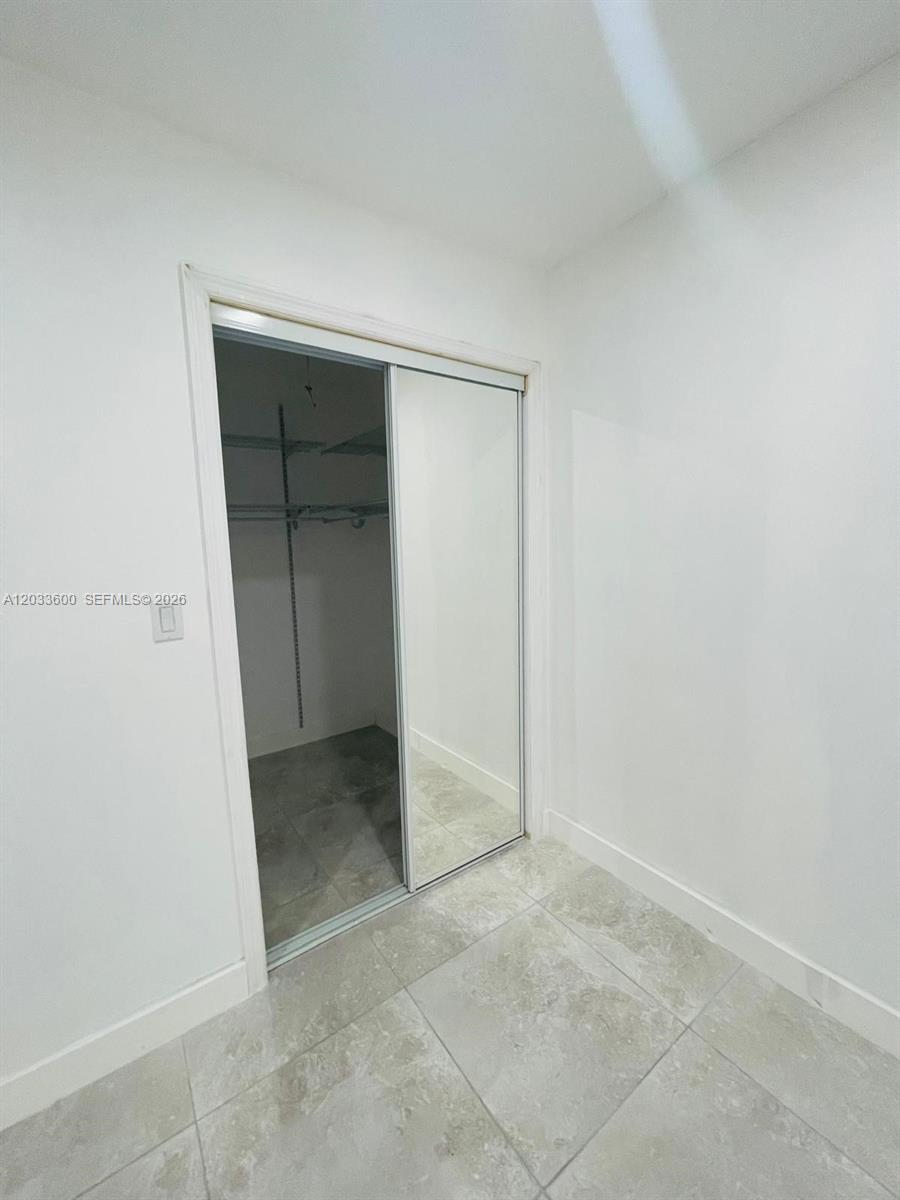 A room with light-colored floor tiles features a closet with sliding mirrored doors — 2437 NW 98th St, Miami FL 33147, MIAMI, FL