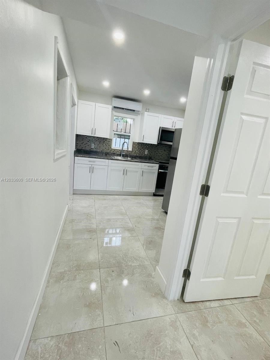 A kitchen with white cabinets, dark countertops, and light-colored tile flooring is viewed from a doorway — 2437 NW 98th St, Miami FL 33147, MIAMI, FL