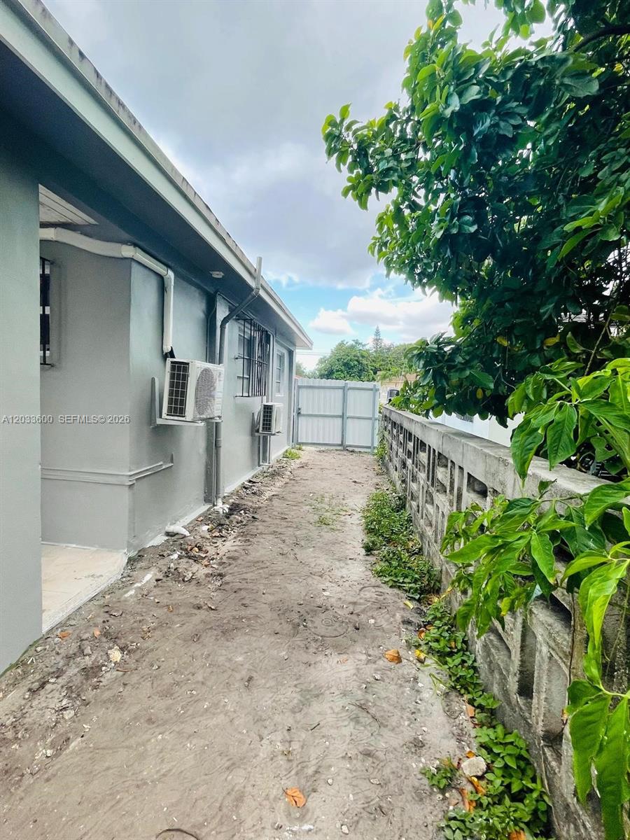A narrow dirt side yard runs between a gray house and a concrete block wall — 2437 NW 98th St, Miami FL 33147, MIAMI, FL