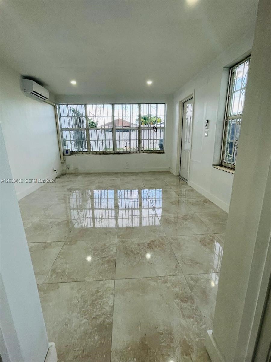 A bright room features large windows with security bars, recessed lighting, and polished tile flooring — 2437 NW 98th St, Miami FL 33147, MIAMI, FL