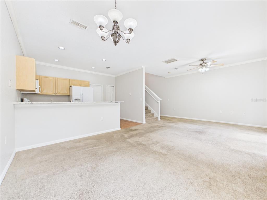 A carpeted living room opens to a kitchen with light wood cabinets and a breakfast bar — 16310 FAIRFORD PALMS COURT, TAMPA, FL