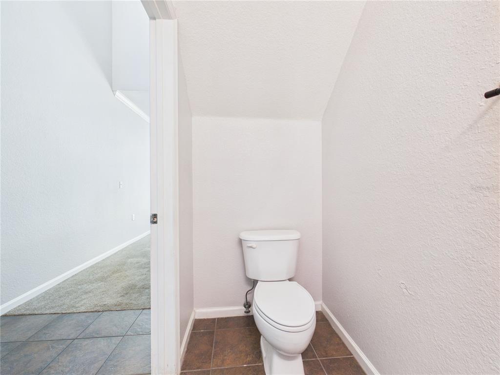 A small bathroom features a white toilet, brown tile flooring, and light-colored walls — 16310 FAIRFORD PALMS COURT, TAMPA, FL