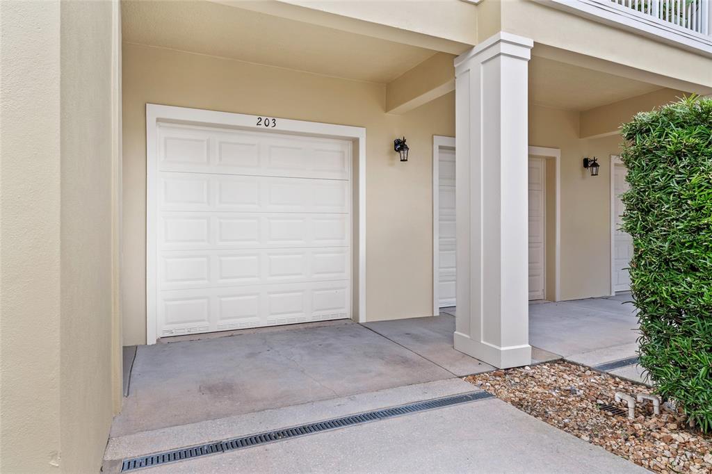A white garage door labeled 203 sits under a covered entryway with a concrete floor — 1819 COMMON WAY ROAD UNIT 203, ORLANDO, FL