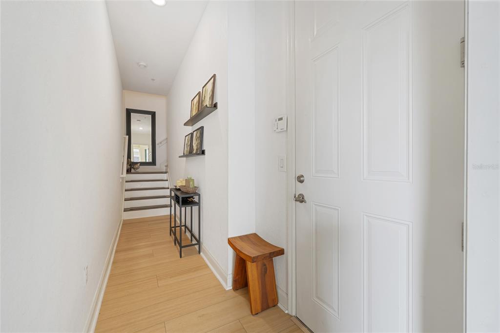 An entryway features light wood flooring, a white door, a wooden stool, and wall shelves — 1819 COMMON WAY ROAD UNIT 203, ORLANDO, FL