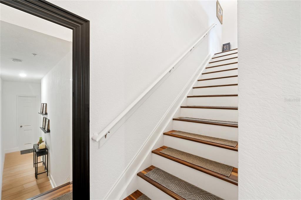 A staircase with wooden treads and carpet runners ascends alongside a white wall and mirror — 1819 COMMON WAY ROAD UNIT 203, ORLANDO, FL