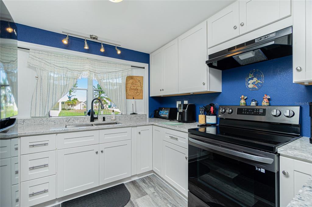 A kitchen features white cabinets, granite countertops, a black stove, and a blue accent wall — 1520 BLUE HERON DRIVE, ENGLEWOOD, FL