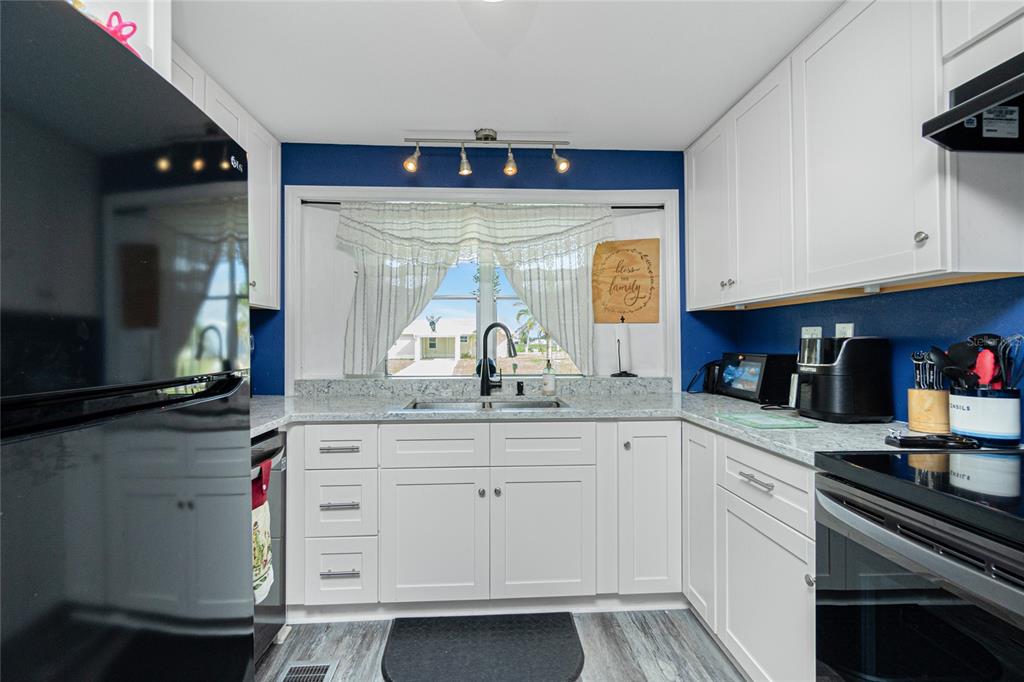 A kitchen features white cabinets, granite countertops, a blue accent wall, and a window view — 1520 BLUE HERON DRIVE, ENGLEWOOD, FL