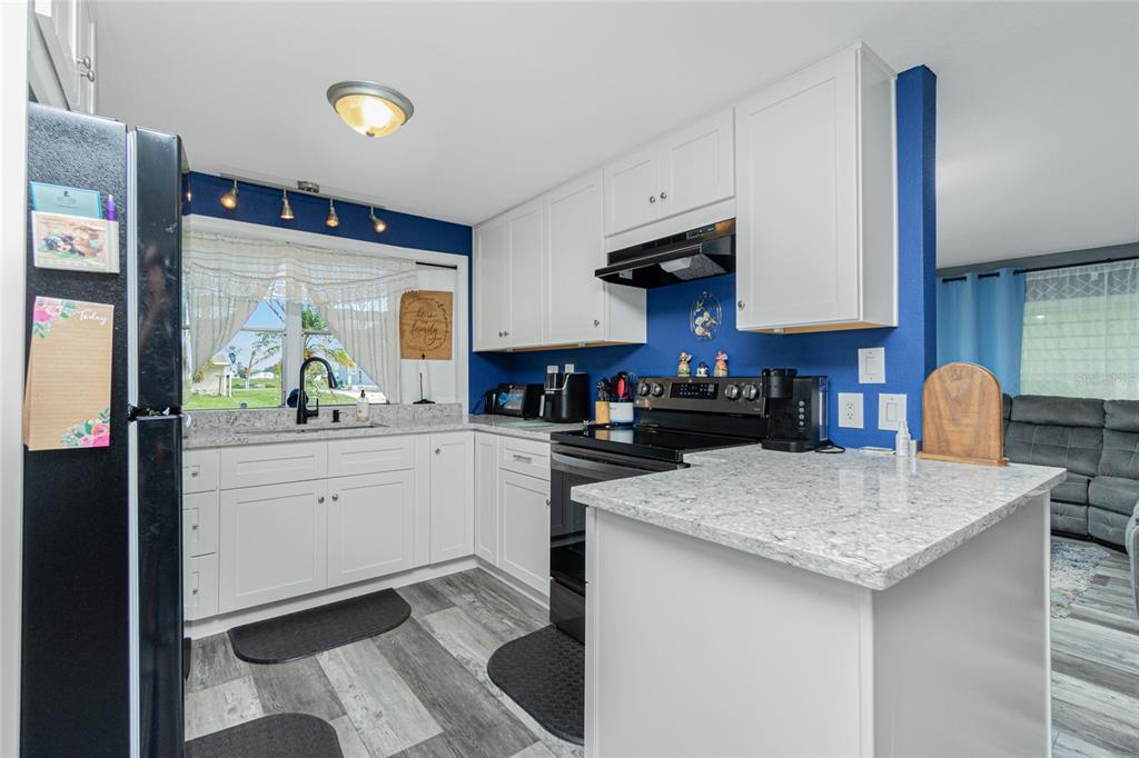 A kitchen with white cabinets, granite countertops, blue walls, and a black refrigerator and stove — 1520 BLUE HERON DRIVE, ENGLEWOOD, FL