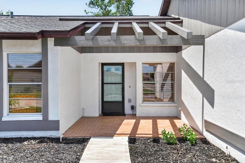 A front exterior view of a house featuring a brick porch and a wooden pergola — 631 FOXWOOD BOULEVARD UNIT 256, ENGLEWOOD, FL