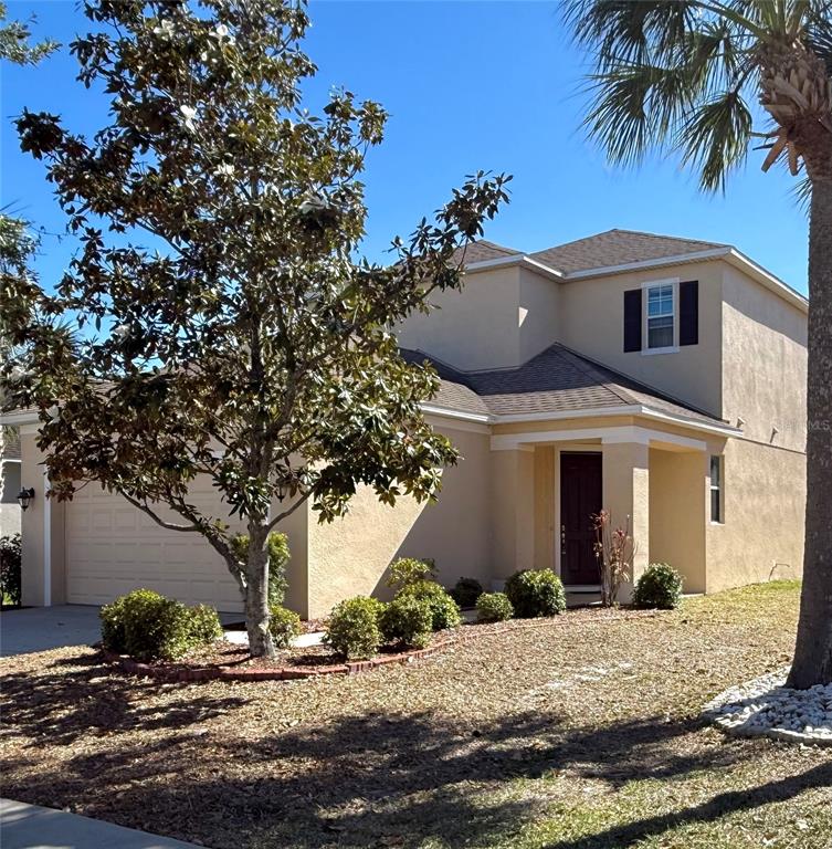 A two-story tan stucco house features a front-facing garage, a covered entryway, and landscaping — 8623 DEEP MAPLE DRIVE, RIVERVIEW, FL