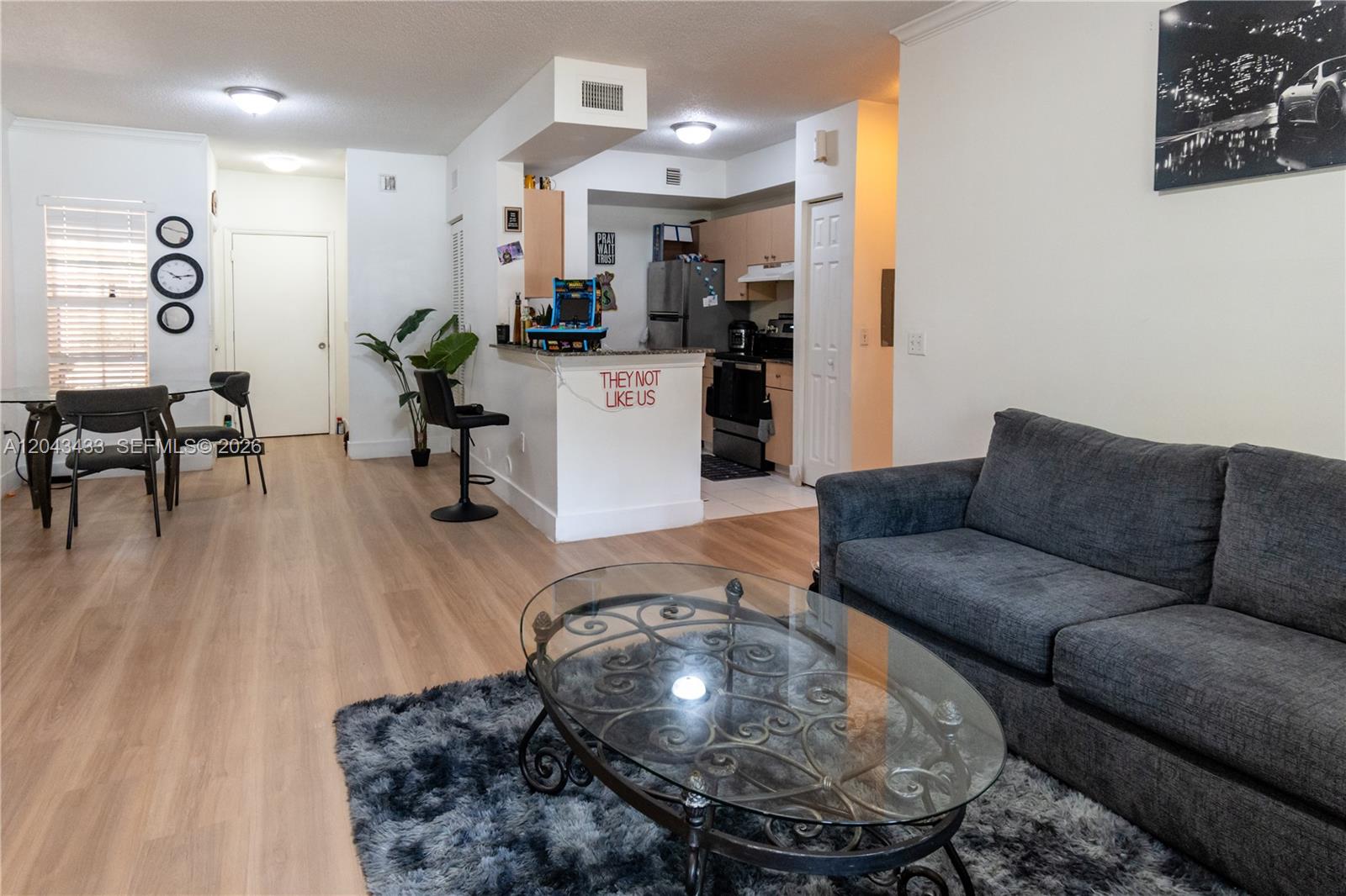 A living room with light wood flooring, a grey sofa, and an open kitchen area — 2482 Centergate Dr # 104, Miramar FL 33025, MIRAMAR, FL