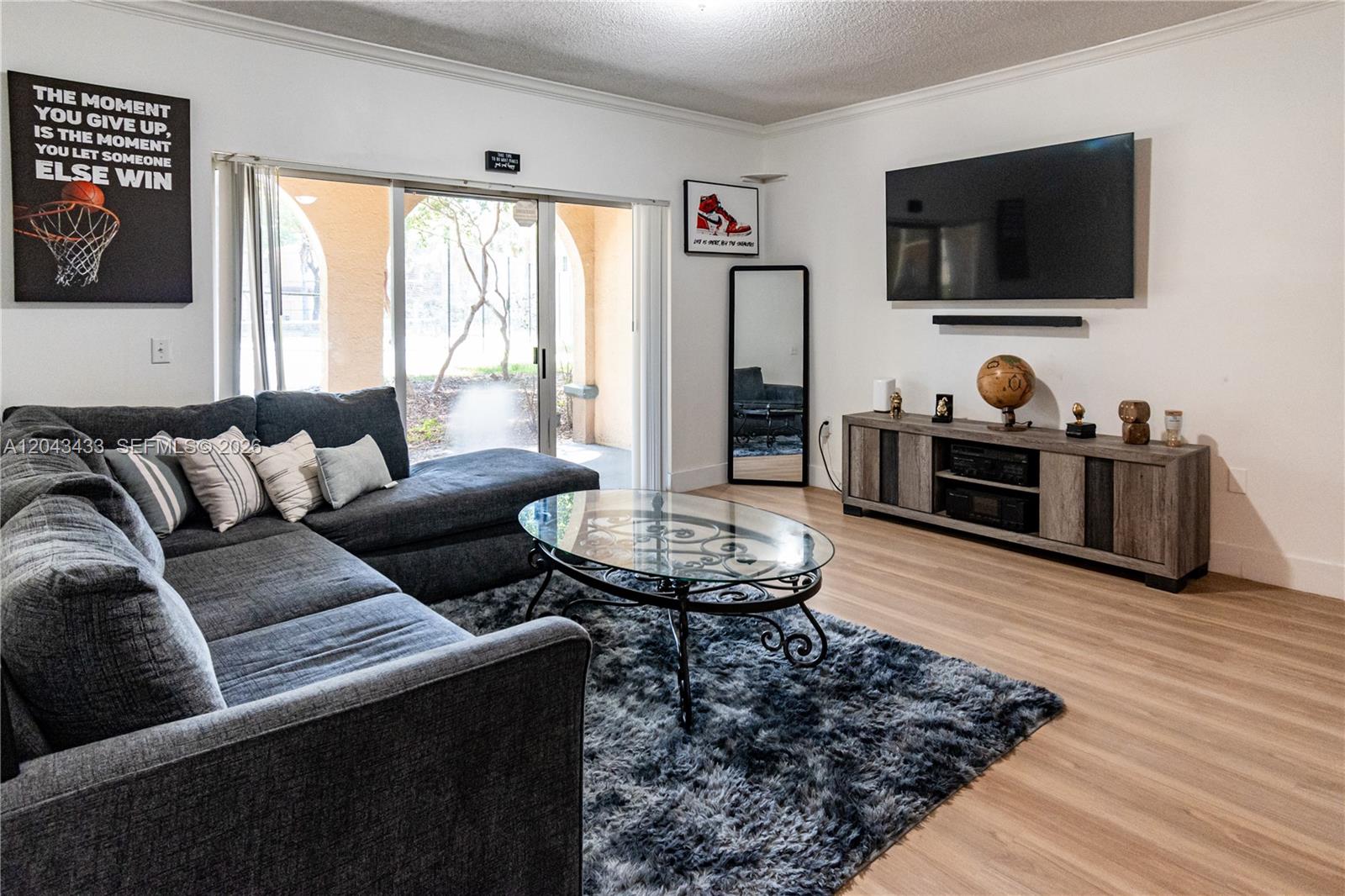 A living room features a gray sectional sofa, glass coffee table, and wall-mounted television — 2482 Centergate Dr # 104, Miramar FL 33025, MIRAMAR, FL