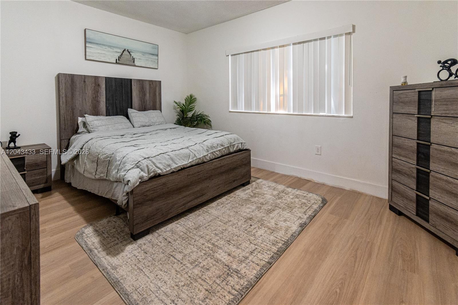 A bedroom features a wood-grain bed frame, matching dresser, nightstand, and a light-colored area rug — 2482 Centergate Dr # 104, Miramar FL 33025, MIRAMAR, FL