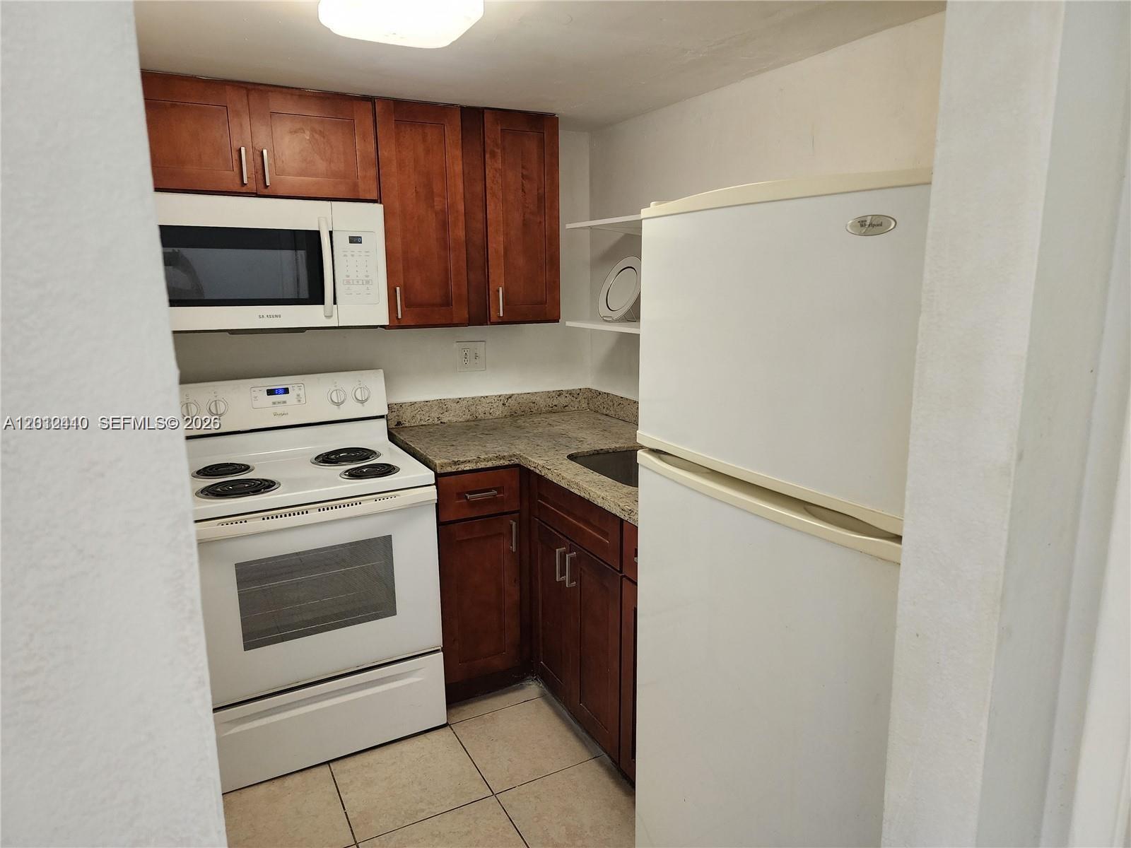 A small kitchen features dark wood cabinets, white appliances, and granite countertops — 241 SE 9th Ave # 103, Pompano Beach FL 33060, POMPANO BEACH, FL