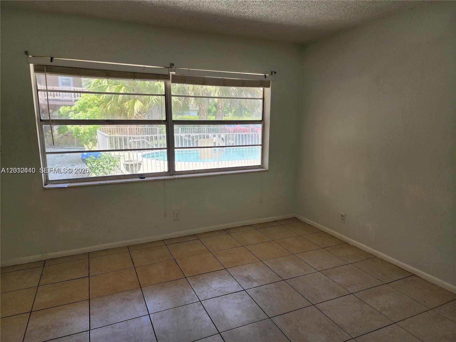 An empty room features beige tile flooring, light-colored walls, and a window overlooking a pool — 241 SE 9th Ave # 103, Pompano Beach FL 33060, POMPANO BEACH, FL