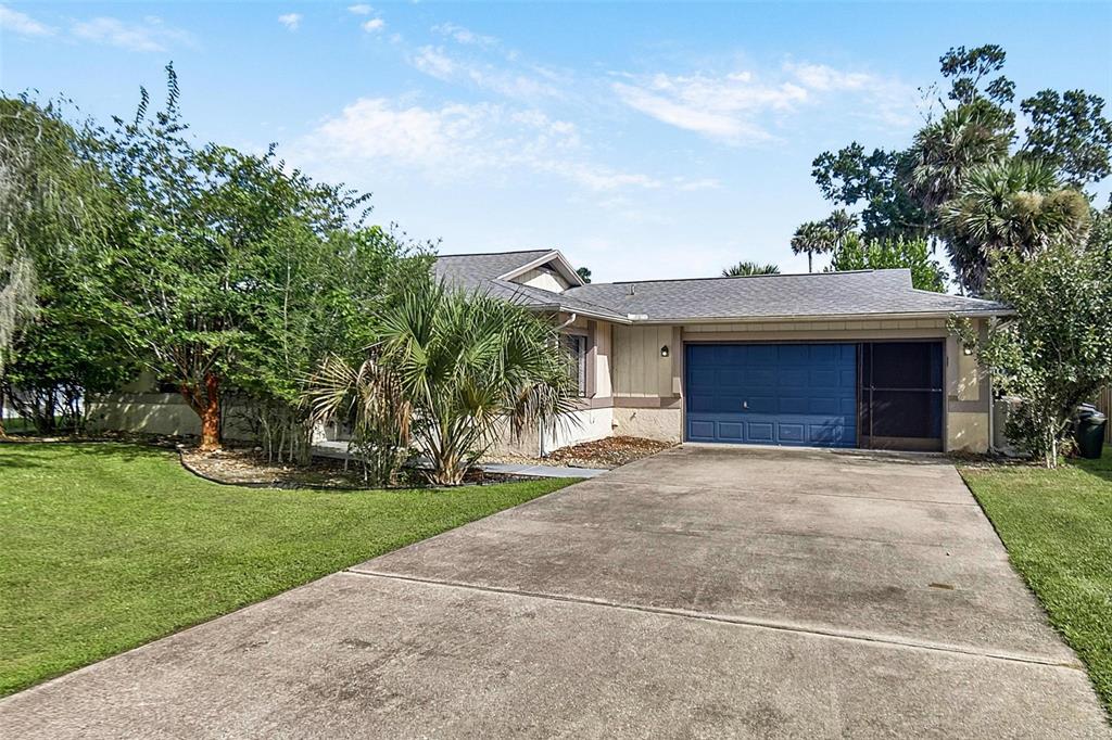 A single-story house features a blue garage door, a concrete driveway, and surrounding trees — 19 BLACKBERRY PLACE, PALM COAST, FL