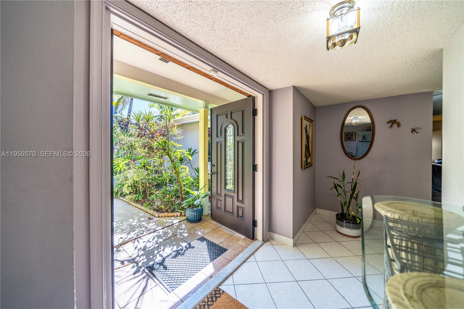 An open front door reveals a lush garden entryway leading into a tiled foyer — 6337 SW 32nd St, Miramar FL 33023, MIRAMAR, FL