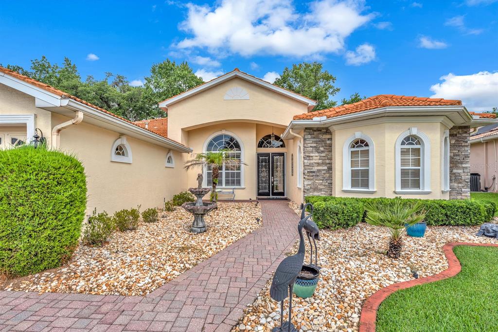 A single-story house with a stone facade, arched windows, and a paved walkway with landscaping — 5151 DELACROIX DRIVE, BROOKSVILLE, FL