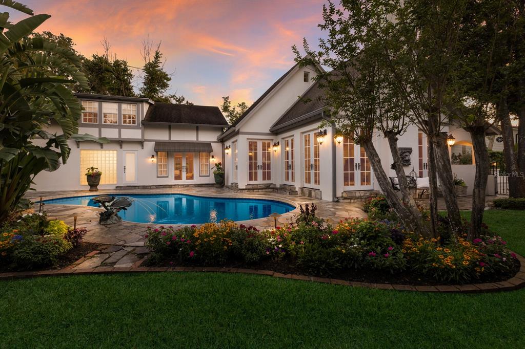 A backyard swimming pool sits in front of a white house with a stone patio — 1829 BOUGAINVILLEA STREET, SARASOTA, FL