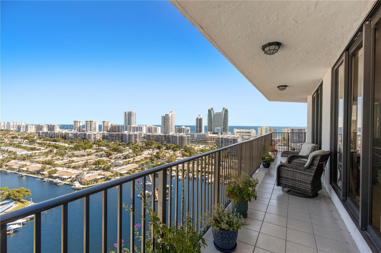 A high-rise balcony features a metal railing, tiled flooring, potted plants, and a waterfront view — 300 Three Islands Blvd, Hallandale Beach FL 33009, HALLANDALE BEACH, FL