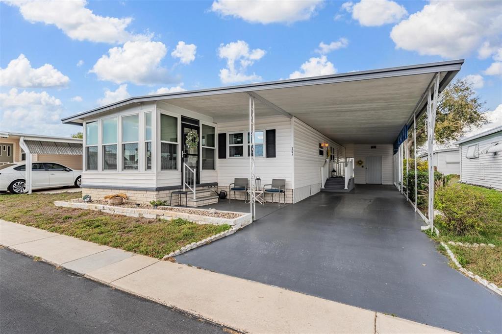 A white manufactured home features a large carport, a front porch, and a paved driveway — 257 SAGO PALM STREET, LARGO, FL