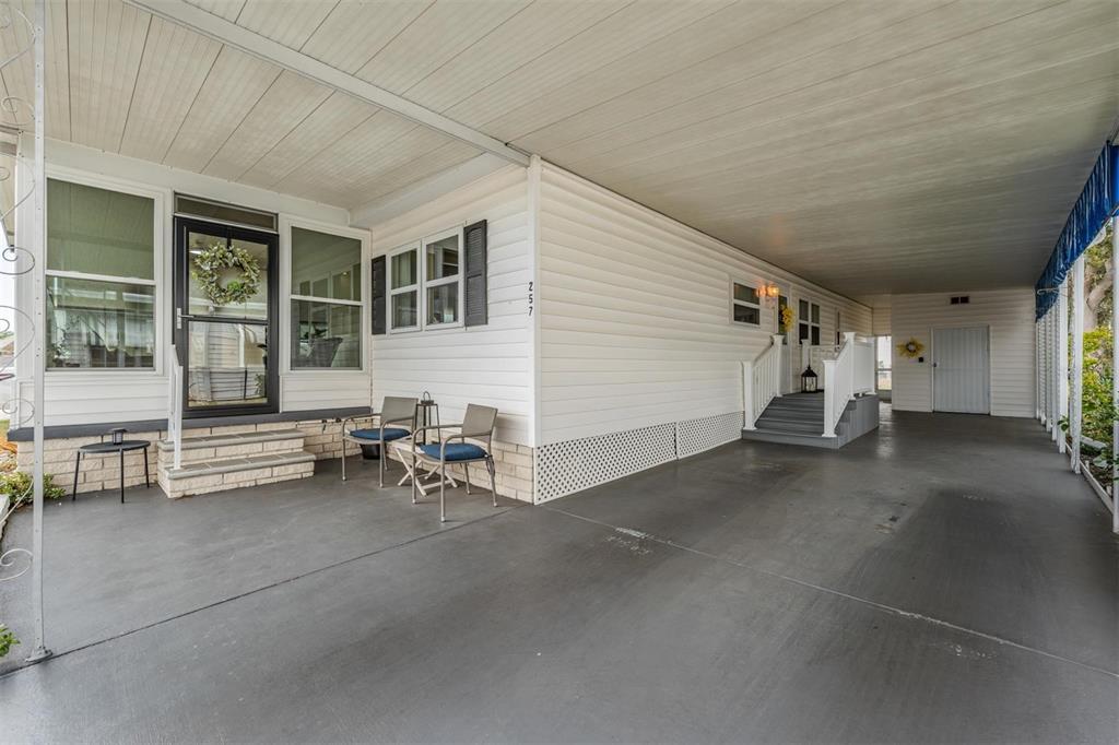 A white manufactured home features a covered carport, a front porch, and gray concrete flooring — 257 SAGO PALM STREET, LARGO, FL