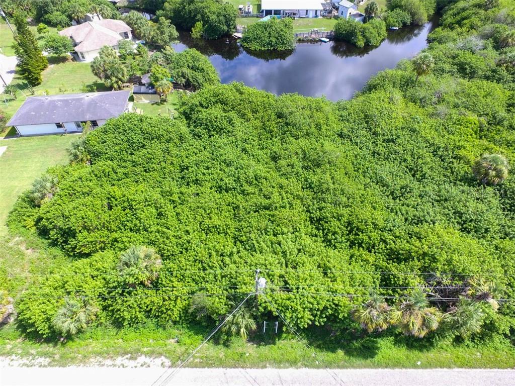 An aerial view shows a densely wooded vacant lot adjacent to a canal and houses — LOTS 15,16,17 SARAGOSSA LANE, NORTH PORT, FL