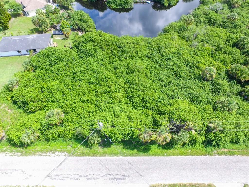 An aerial view shows a dense, tree-covered vacant lot adjacent to a pond and road — LOTS 15,16,17 SARAGOSSA LANE, NORTH PORT, FL