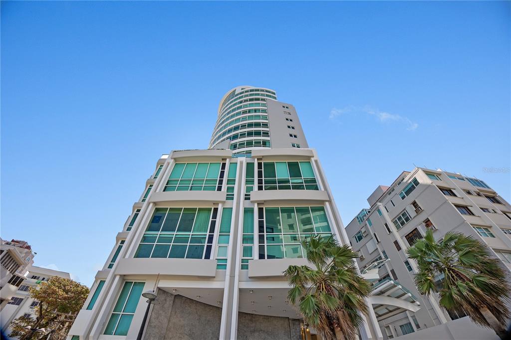 A low-angle view of a modern high-rise building with glass windows and palm trees — 1052 ASHFORD AVE UNIT 9B, SAN JUAN, PR