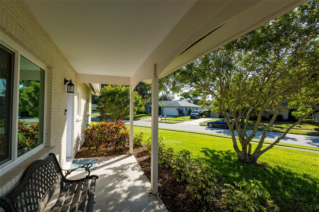 A covered front porch features a metal bench, brick siding, and a view of the street — 3005 CHASE CIRCLE, SARASOTA, FL