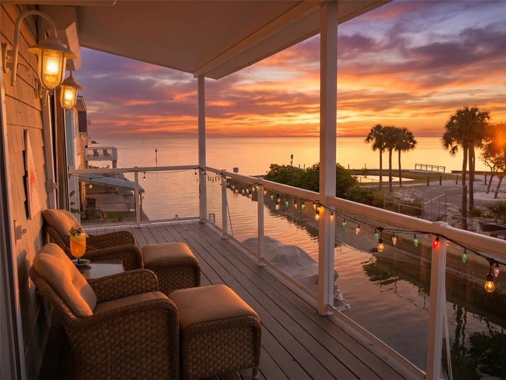 A wooden balcony with wicker chairs overlooks a canal and the ocean at sunset — 6249 LONNIE LEE LANE, HUDSON, FL