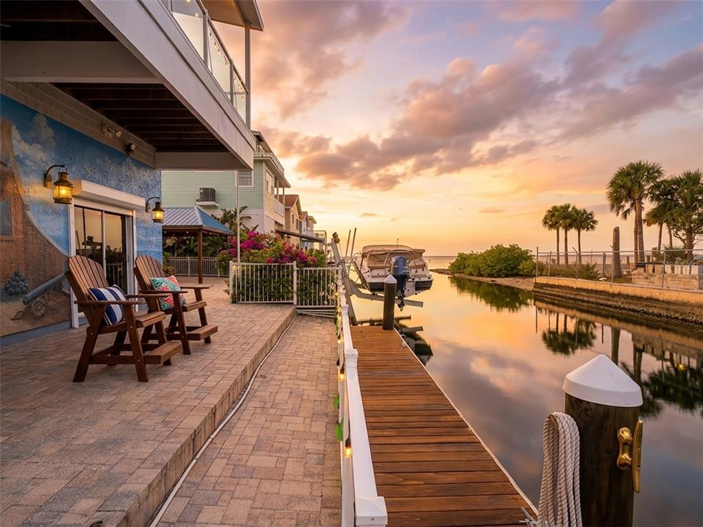A paved patio with two wooden chairs overlooks a canal, a boat dock, and sunset — 6249 LONNIE LEE LANE, HUDSON, FL