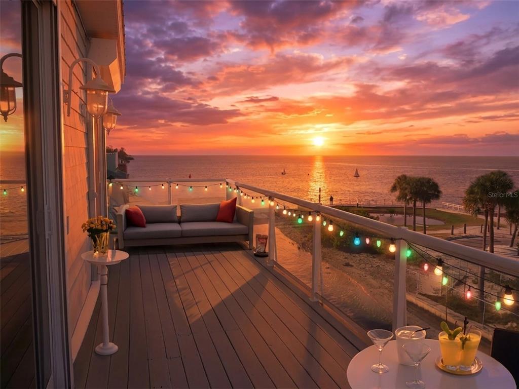 A balcony with a gray sofa, string lights, and a table overlooking a sunset ocean view — 6249 LONNIE LEE LANE, HUDSON, FL