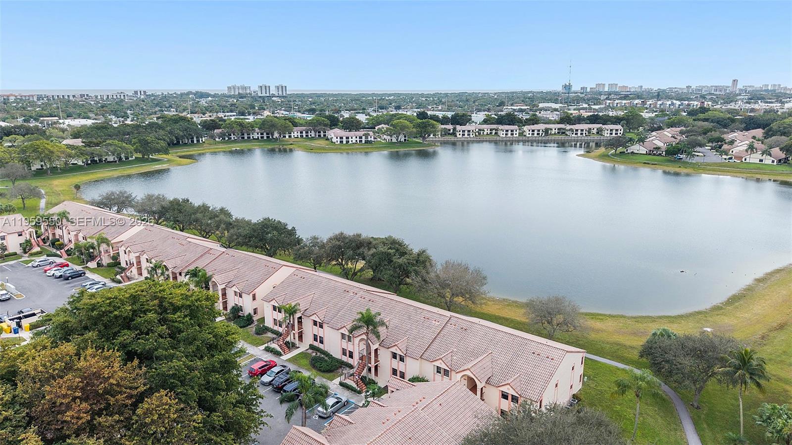 An aerial view shows a multi-story residential building complex situated beside a large lake — 3150 Leewood Ter # L124, Boca Raton FL 33431, BOCA RATON, FL
