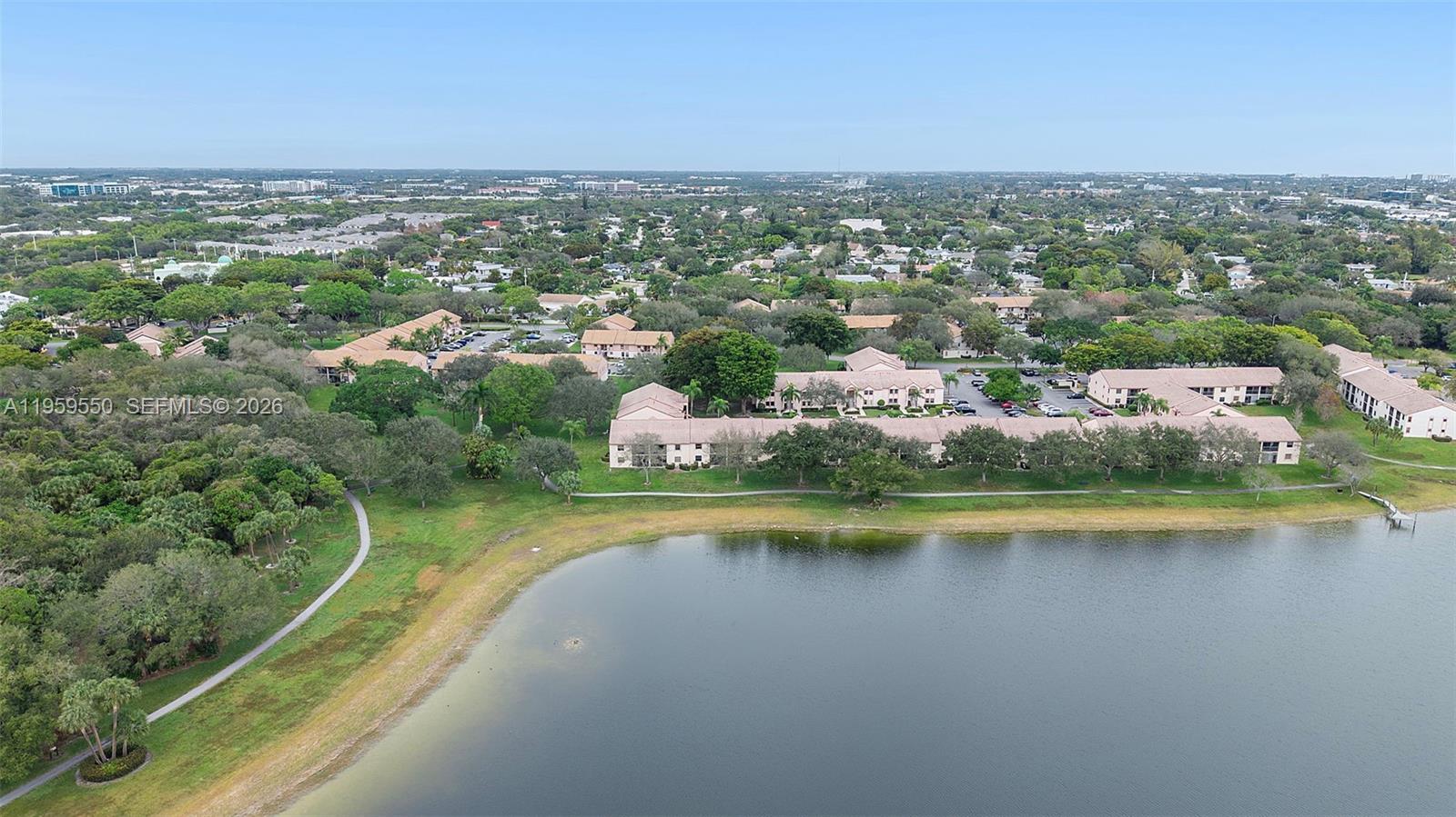 An aerial view shows a residential complex situated along a lake with surrounding green space — 3150 Leewood Ter # L124, Boca Raton FL 33431, BOCA RATON, FL
