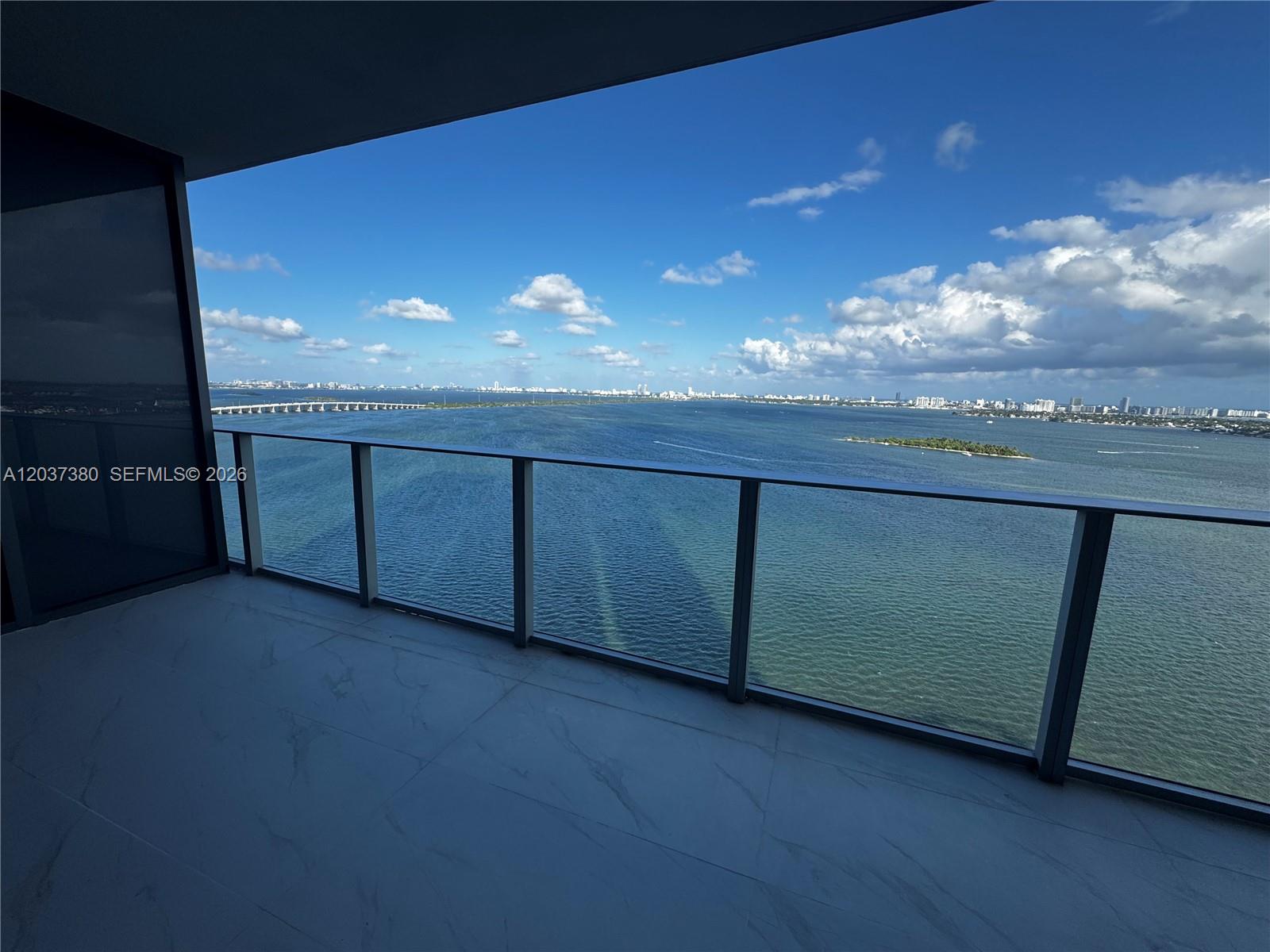 A balcony with marble-look tile flooring overlooks a body of water and a distant city — 700 NE 23 # 2206, Miami FL 33137, MIAMI, FL