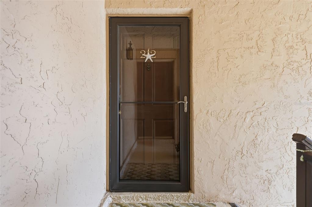 A dark-framed storm door with a decorative starfish accent sits in a textured stucco wall — 212 CEDARWOOD CIRCLE UNIT 212, SEMINOLE, FL