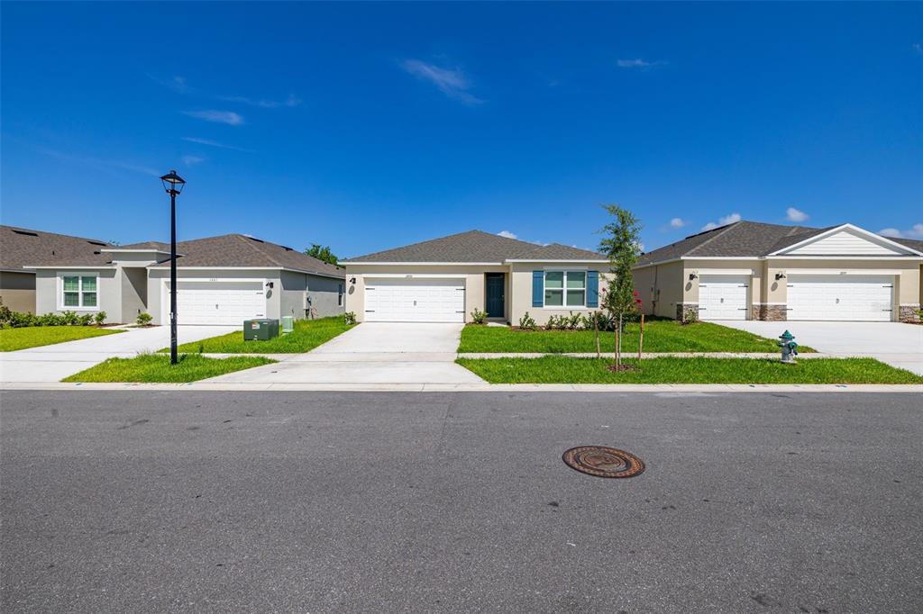 A street view of three single-story suburban houses with attached garages and green lawns — 2893 HOUSE FINCH ROAD, HARMONY, FL